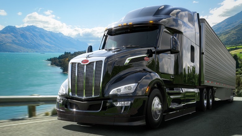 Black Peterbilt 579 driving with a lake in the background
