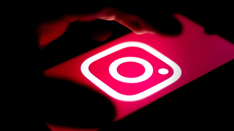 A hand hovers over a phone displaying the Instagram logo
