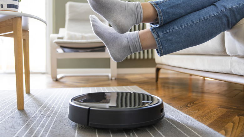 A woman lifting her feet off the floor to allow a robot vacuum to work underneath her