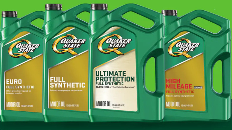 Several 5-quart bottles of various Quaker State oil products on a green background.