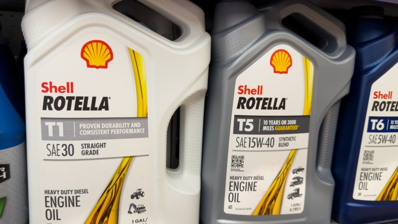 Three 5-quart bottles of Shell Rotella oil sitting on a store shelf.