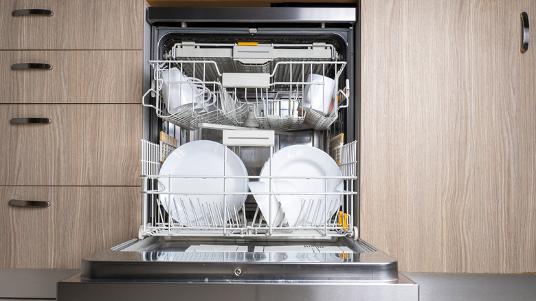 A close-up of an open door of built-in dishwasher in the kitchen, with plates and dishes inside.