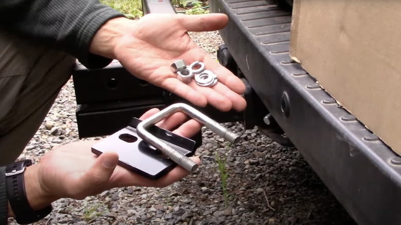 A person is holding a hitch clamp in one hand and fasteners and bolts in the other.