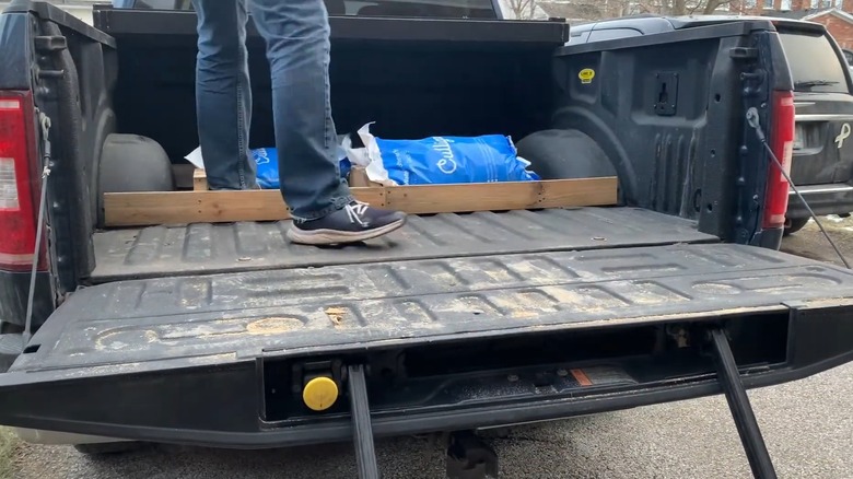 A man adding bags of rock salt to a pickup bed securing them in place with a modified pallet.