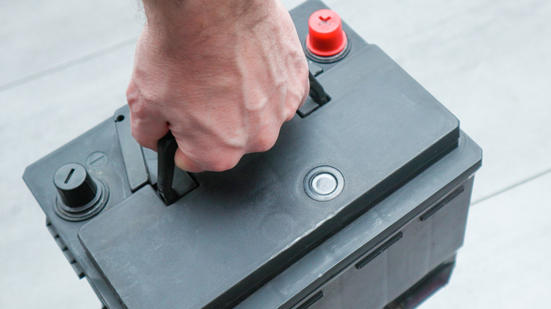 A person holding a car battery.