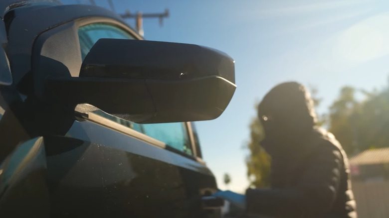 Hooded adult breaking into a black vehicle