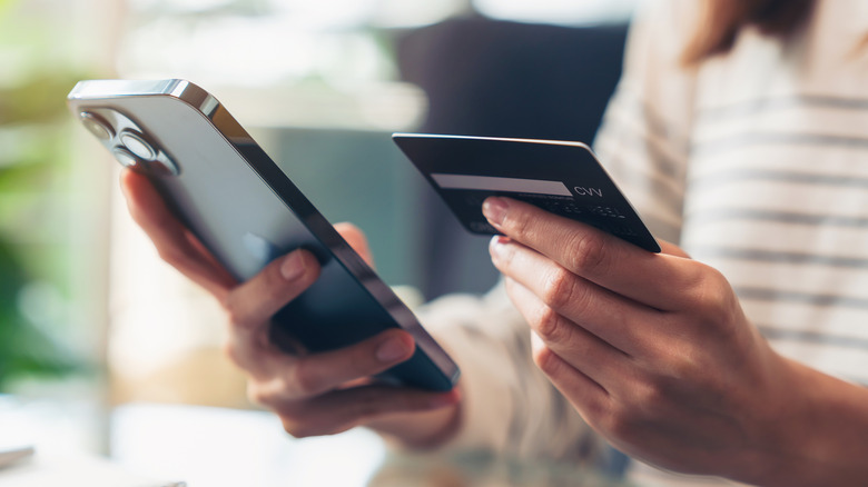 a faceless woman is holding an iphone and a credit card