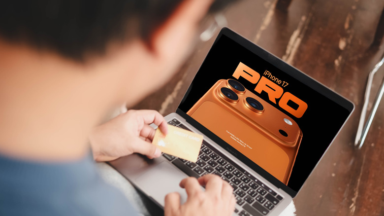 a man is holding up a credit card while looking at an iphone 17 pro max ad on his laptop