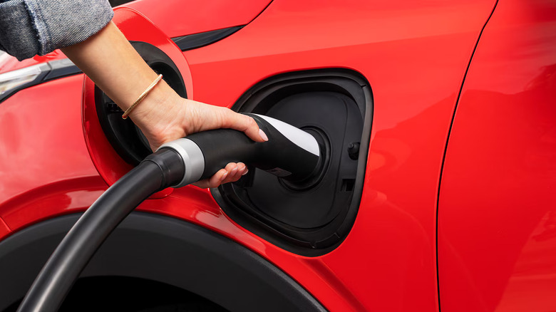 close-up of a person's hand plugging a charger into a red 2027 Chevrolet Bolt RS