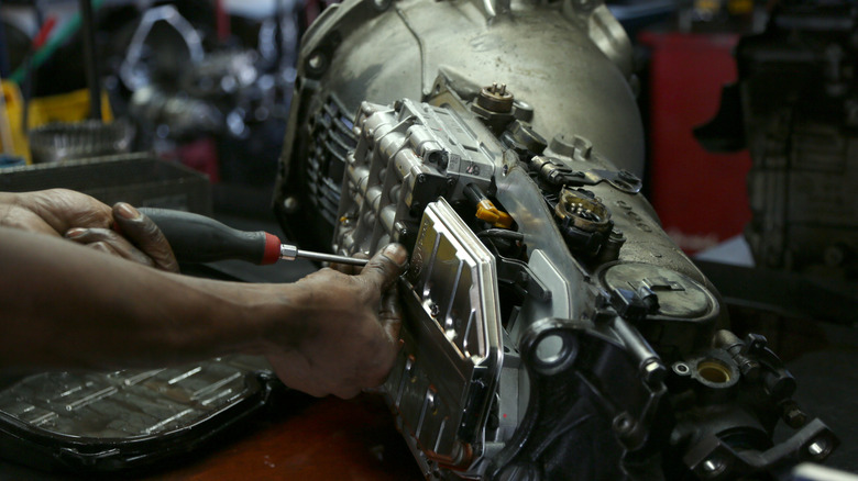 Mechanic disassembling fluid pan of automatic transmission removed from vehicle