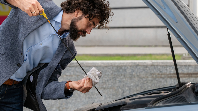 Bearded man in smart casual attire inspects his car's oil level