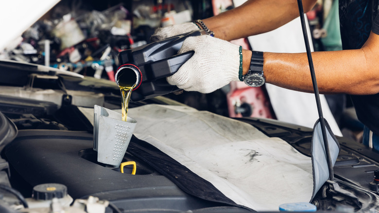 Car mechanic replacing and pouring fresh oil into engine