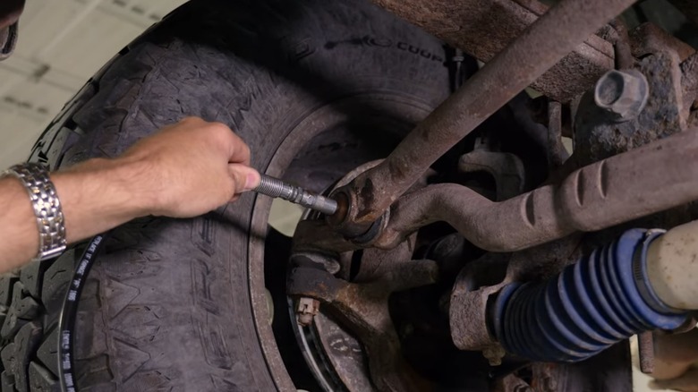 A person using a grease gun to grease a suspension system component