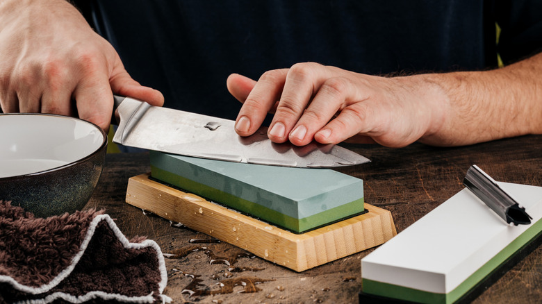 A man sharpens a knife with a grindstone