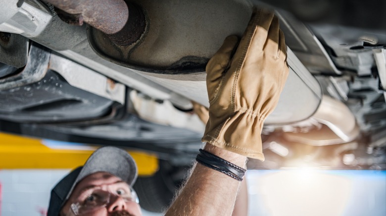 mechanic inspecting a catalytic converter under a car