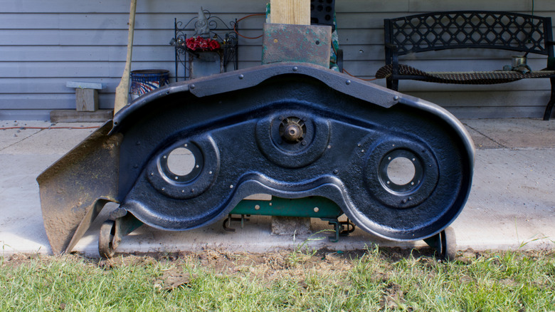 A painted underside of a mower deck exposed on its side in a yard