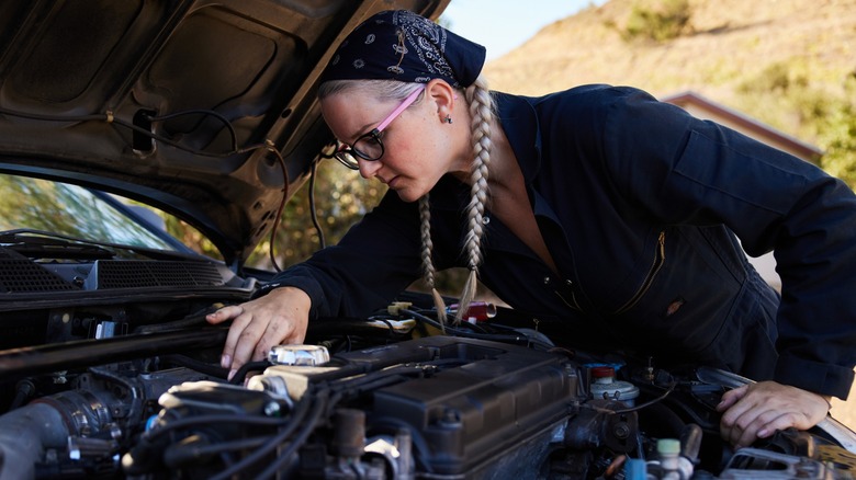 A woman peering into the component of an engine bay