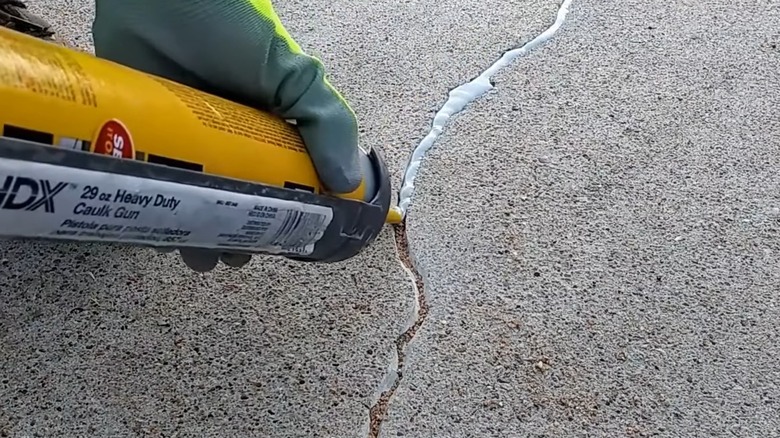 A person filling a crack in a concrete driveway.