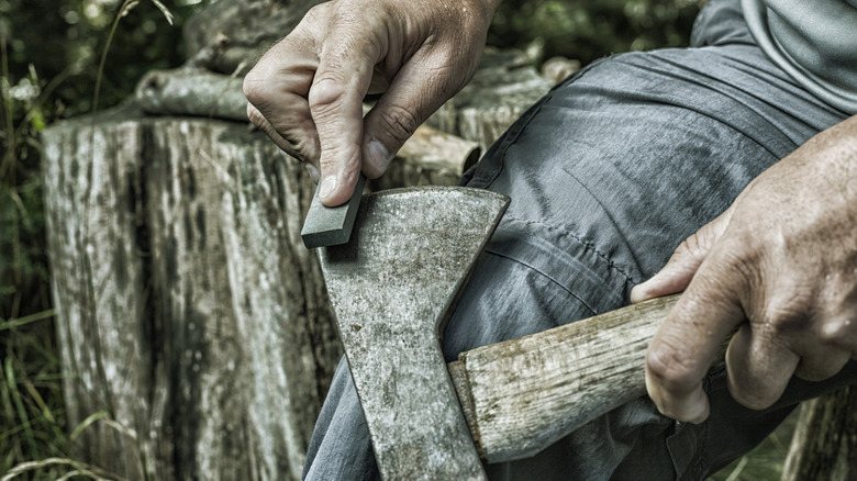 A man's hands sharpening an old, rusty axe