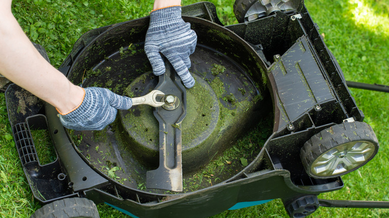 A person fixing a lawn mower blade with wrench, on a flipped over lawn mower