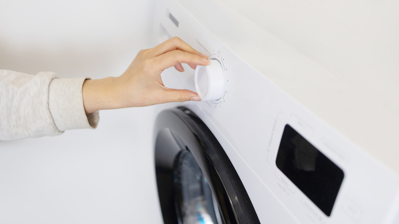 Close-up of a person's handing turning the control knob on a front-loading washing machine