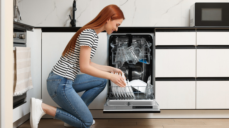 a woman loading plates into a full dishwasher