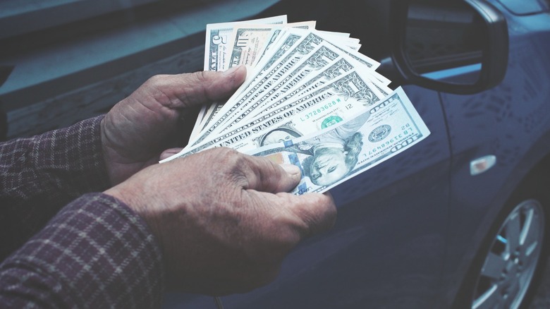 Man's hands holds a wad of cash next to a car