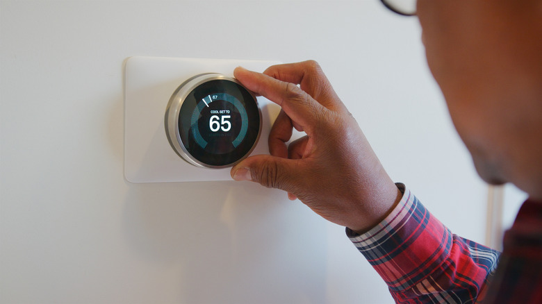 person adjusting the temperature on a smart thermostat mounted on a white wall