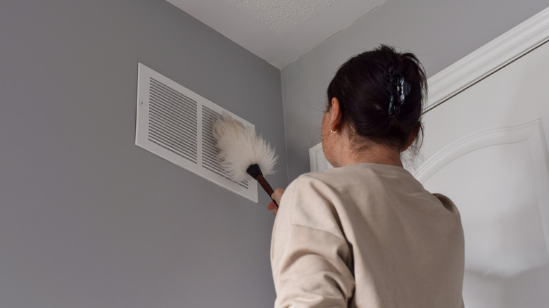 Woman cleaning return air vents with a duster inside her home,