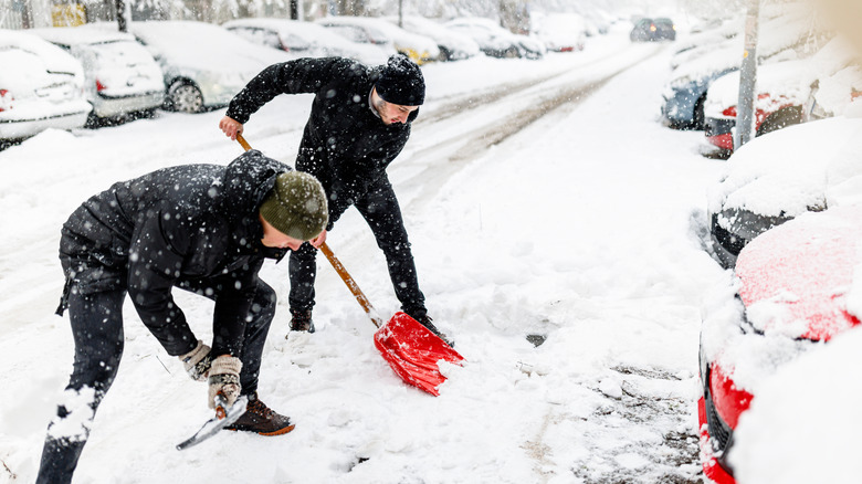 Two men using snow shovels to clean up the deep snow in front of car.