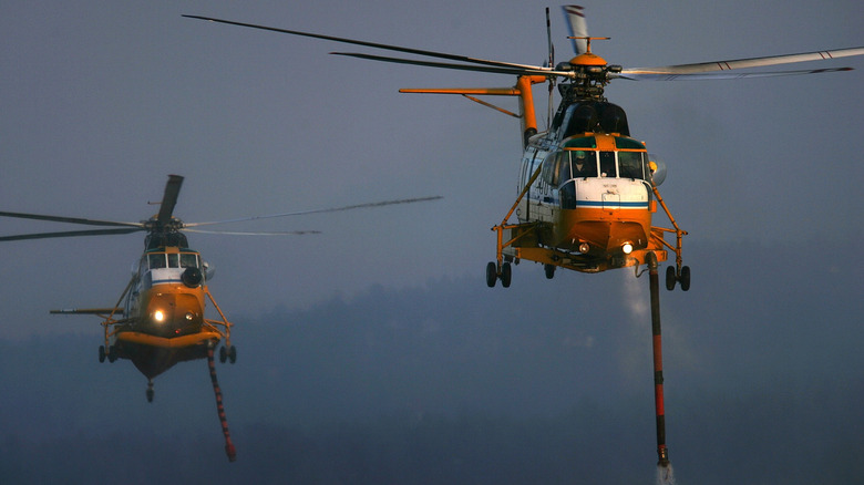 A pair of orange and white S-61s modified to fight fires with fore-mounted waterspouts pointed towards the ground