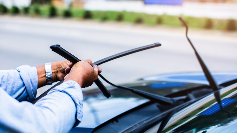 A person changing car wiper blades at the side of the road.