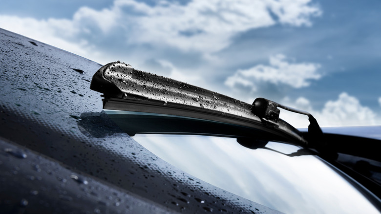 A singular wet windshield wiper pictured under cloudy skies.