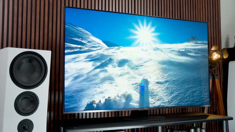 A Hisense U8QG television showing a snowy mountain scene, white home theater speaker next to it