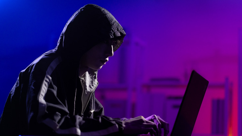 A person in a dark hoodie using a laptop representing a hacker