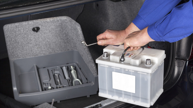 A man replacing a car battery located in the trunk