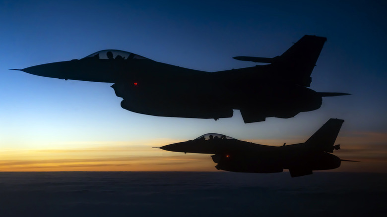 Two F-16s fly in tandem at twilight.