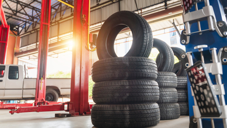 Tires stacked inside of repair shop with sun coming through garage door opening.