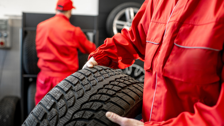 Close up view of man in red suit carrying a tire inside a tire shop.