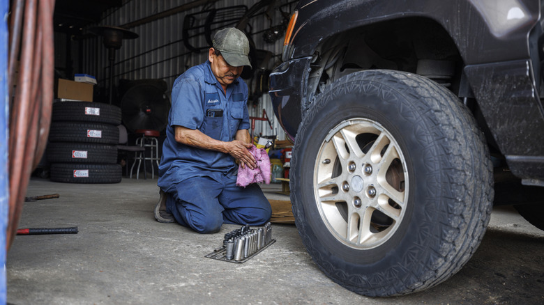 A mechanic in blue suit inspecting the tire of an SUV.