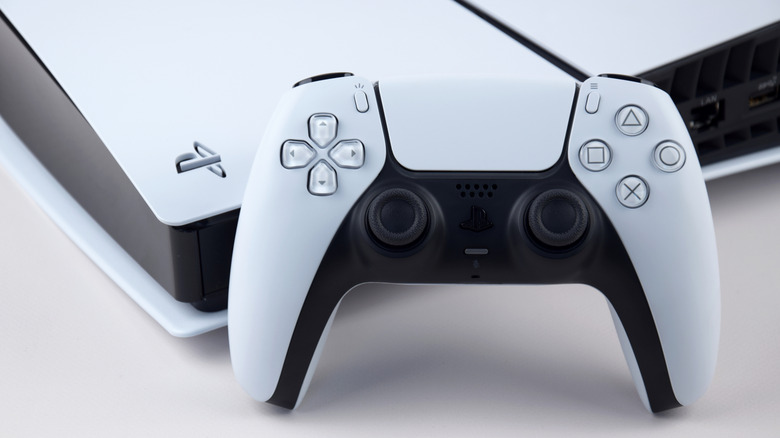 A Sony PlayStation 5 sitting flat on a table with a white PS5 controller leaning against it