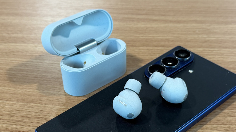 White Sony WH-1000XM6 wireless earbuds and a Samsung smartphone on a wood table