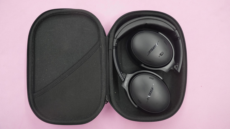 A pair of Bose QuietComfort 45 headphones in their open case on a flat, pink back drop.