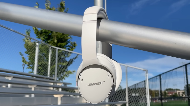 A pair of cream Bose QuietComfort 45 headphones hanging on a hand railing in a public park, blurred back drop.
