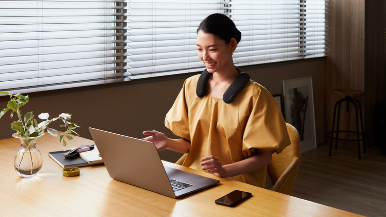 Woman wearing Sony BRAVIA U neckband speakers while at desk with laptop