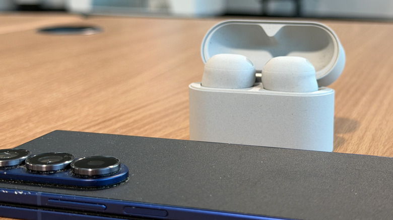 Sony WF-1000XM6 earbuds on a table with a phone in the foreground