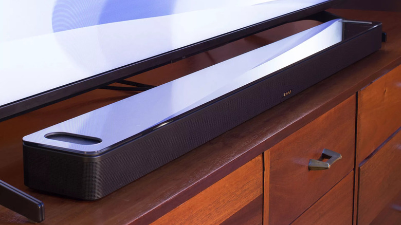 A soundbar placed on a wooden TV furniture with shelves.