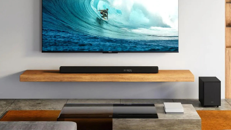 A Dolby Atmos soundbar placed on a wooden shelf under a wall-mounted TV.