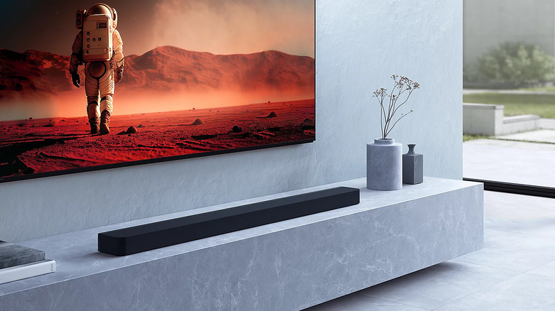A TV mounted on the wall, with a soundbar and a vase placed under it.