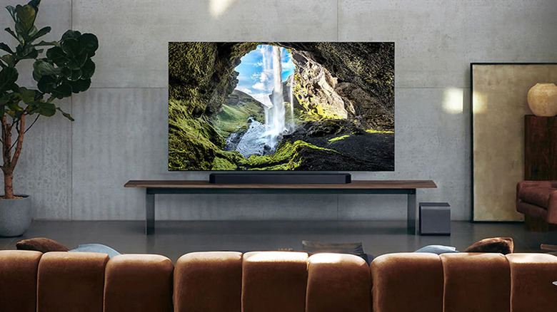 A TV with a soundbar next to it in a living room with a plant.